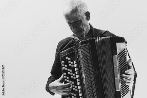 Monochrome portrait of seniot man, retro musician playing the accordion isolated on white background. Concept of art, music, style, older generation, vintage photo