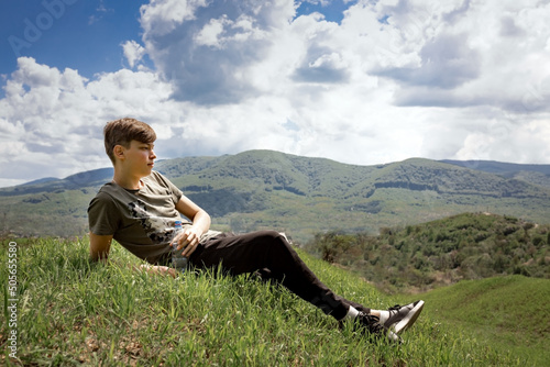 The guy lays on top of the mountain and looks at the landscape. He is holding a bottle of water in his hand. Rest. relax. Summer vacation. Camping.
