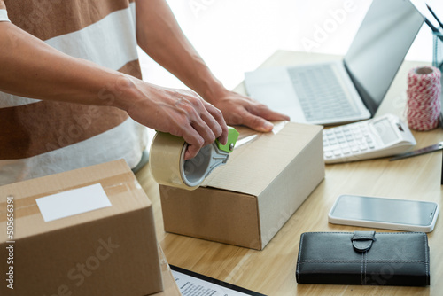 Online shopping concept the shop seller sealing the parcel of his goods on the desk