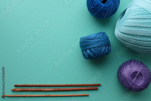 Set of crochet hooks and skeins of cotton yarn on a green background.