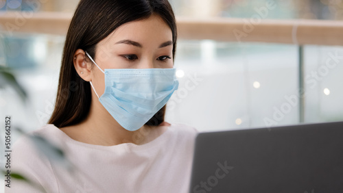 Asian student Korean business woman in medical face mask freelancer writer journalist typing working laptop using free Wi-Fi studying with computer app e-learning distant education pandemic e-commerce