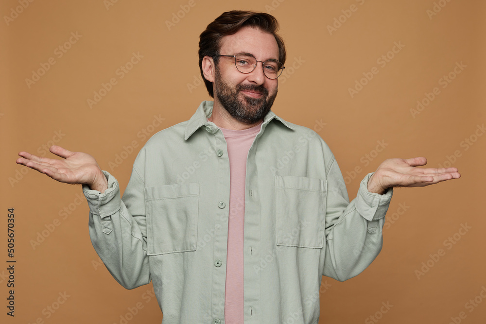 Studio portrait of bearded man standing over beige background wears casual shirt and glasses raised his hands with confused facial expression Studio portrait of bearded man standing over beige background wears casual shirt and glasses raised his hands with confused facial expression