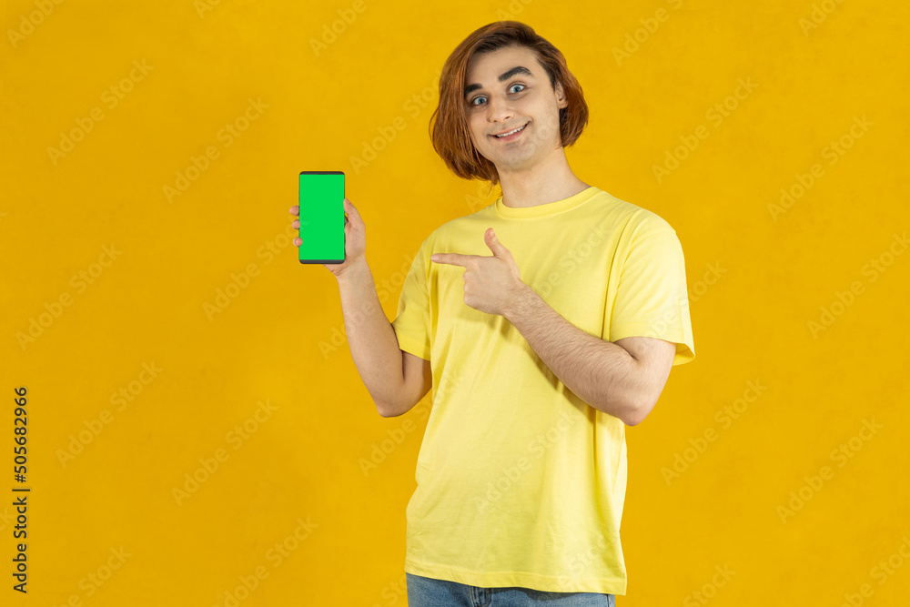 Young man Prep Student with long hair. 20s guy with smartphone on a yellow background Young man Prep Student with long hair. 20s guy with smartphone on a yellow background