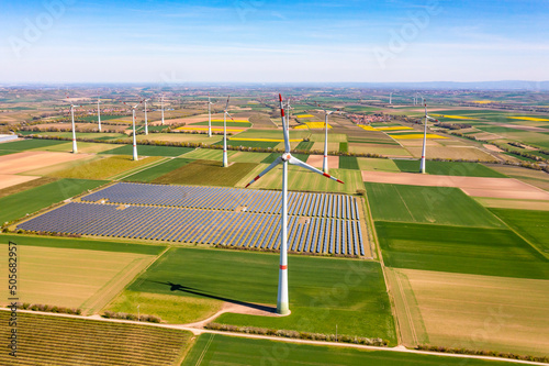 Panorama of solar panels of a solar park amidst wind turbines between agricultural fields photo