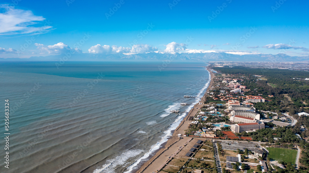 Fototapeta premium Drone view of the sea coast in Belek, Antalya, Turkey. Mountains with snow caps, clouds and sunlight over the sea. Aerial footage over the Mediterranean coast
