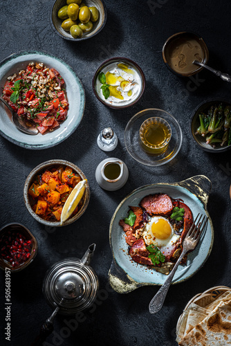 Turkish breakfast table. Flat-lay pastries, vegetables, greens, olives, cheeses, fried eggs, spices, jams, honey, tea in copper pot and tulip glasses