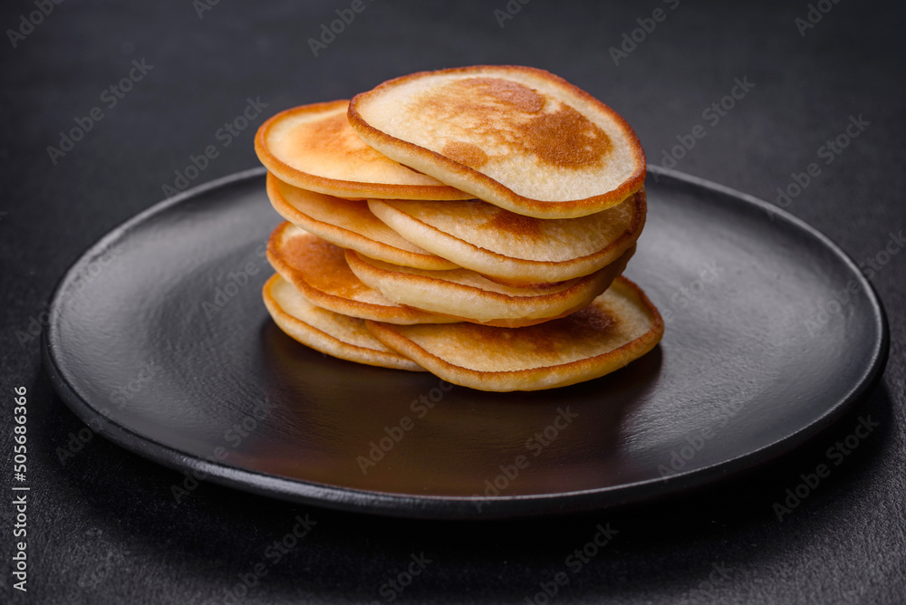 Delicious fresh pancakes on a black plate against a dark concrete background Delicious fresh pancakes on a black plate against a dark concrete background