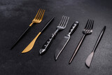 Several knives and forks in black gold and silver on a dark concrete background