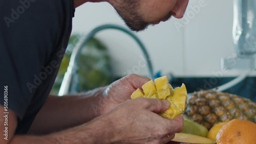 Hungry man gobbles mango on the kitchen