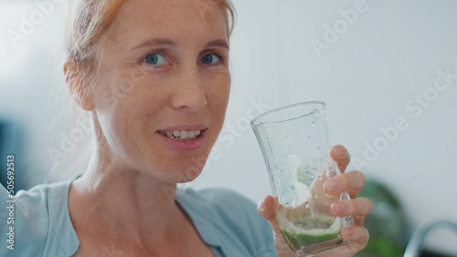 Healthy drink. Redhead woman drinks healthy green cocktail on the modern kitchen photo