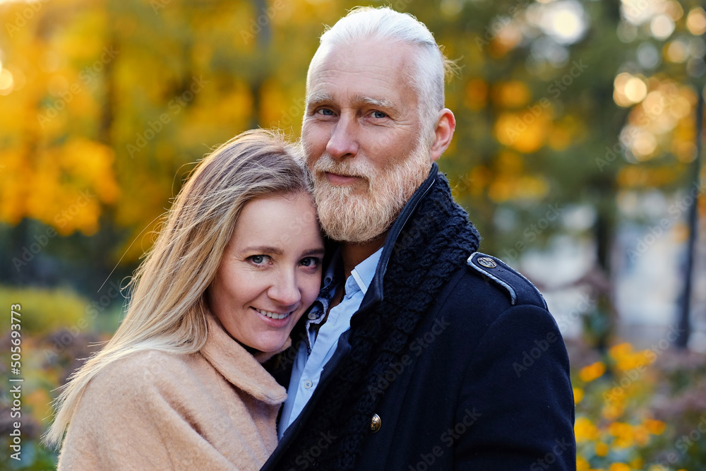 Portrait of hugging elderly man and young woman looking at camera outdoors in fall.