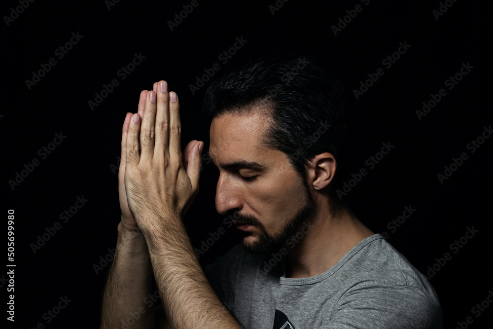 The man folding his hands in prayer to god on a black background. prayer to God for happiness and a better life. Repent of your sins. Unity with God The man folding his hands in prayer to god on a black background. prayer to God for happiness and a better life. Repent of your sins. Unity with God