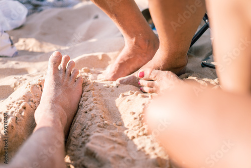 close up of the feet of two unrecognizable people on the sand of the beach. One of them has her toenails painted pink. summer concept.