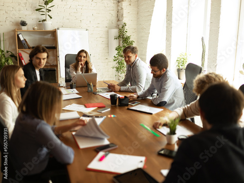 Working process at modern business company. Young men and women discussing something with coworkers, sitting at office table. Concept of team, job, career
