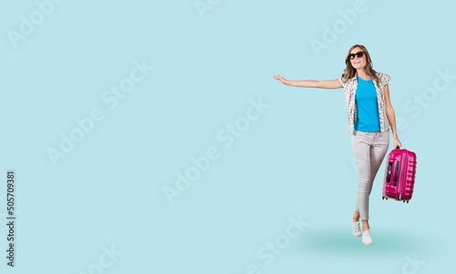 Happy american young woman tourist in casual outfit holding suitcase over blue pastel, traveling concept.