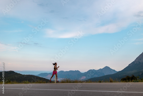 A girl runs along an asphalt road against the backdrop of beautiful mountains