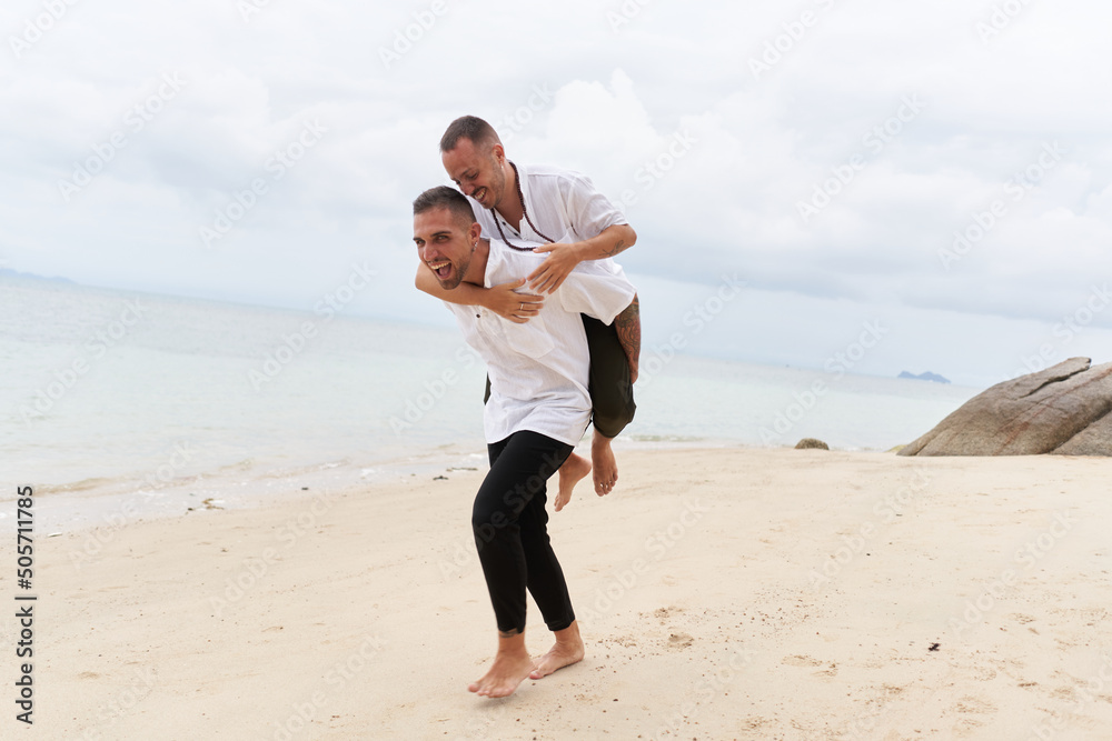 Man piggybacking his gay partner on a beach Man piggybacking his gay partner on a beach