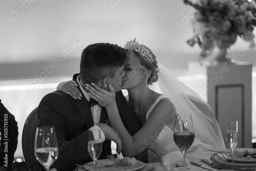 An elegant wedding couple kissing ardently. The bride is blonde and the groom is in a blue suit. Black and white image