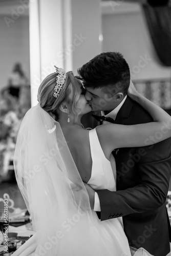 An elegant wedding couple kissing ardently. The bride is blonde and the groom is in a blue suit. Black and white image
