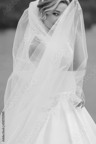 Expressive portrait of a charming bride with a beautiful veil. The girl covered her face with a veil. Black and white image.