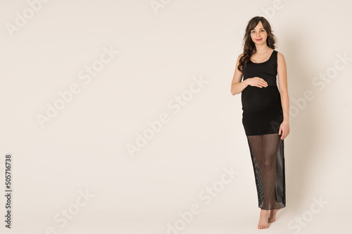 Portrait shot of a young beautiful woman in the second trimester of pregnancy on a monochrome background. Close-up of a pregnant woman in casual clothes with her hands on a round stomach. The concept