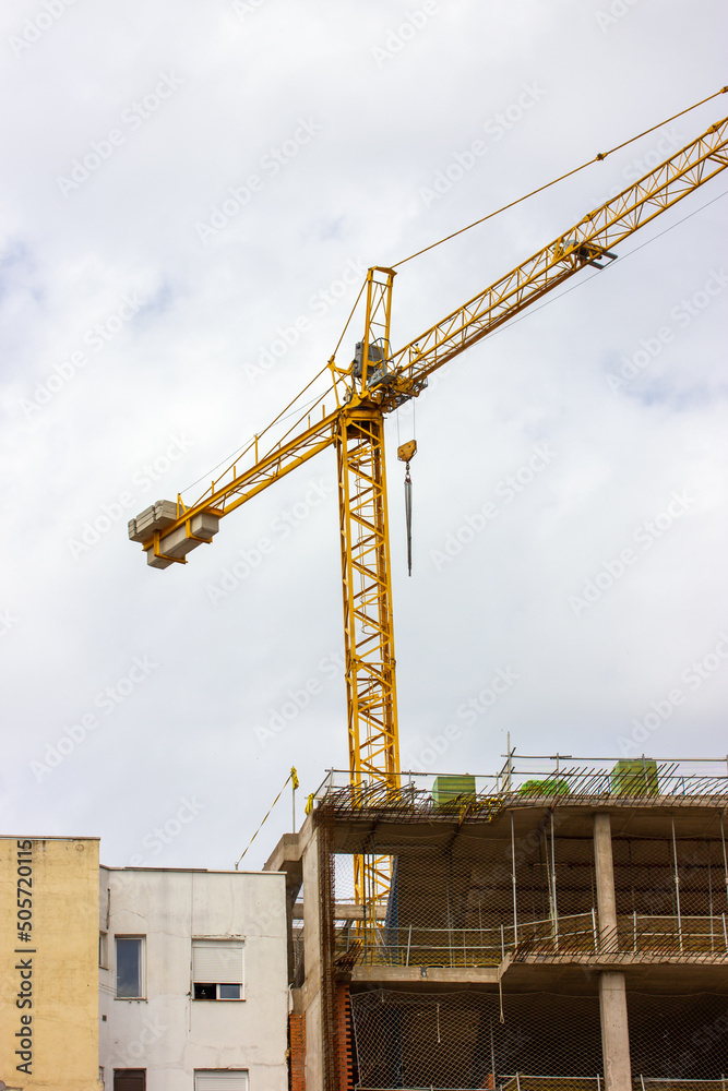 The facade of a residential multistory panel building that is being built in the city. Scaffolding, construction crane in a background. Construction business. Investing in real estate housing concept.