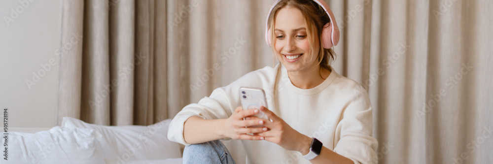 Young woman in headphones using cellphone and laptop in bedroom Young woman in headphones using cellphone and laptop in bedroom