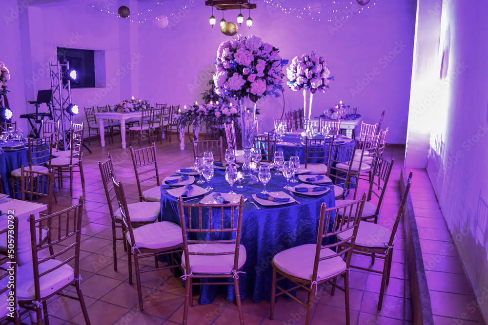 wedding party, full of flowers chandeliers, decorations, candles hanging balloons, plates on the table, hall decorated for event.
Wedding hall, with lights on the ceiling, decorated tables, with plate