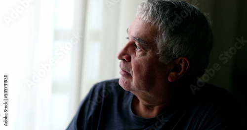 Middle aged man in crisis sitting at home looking through window