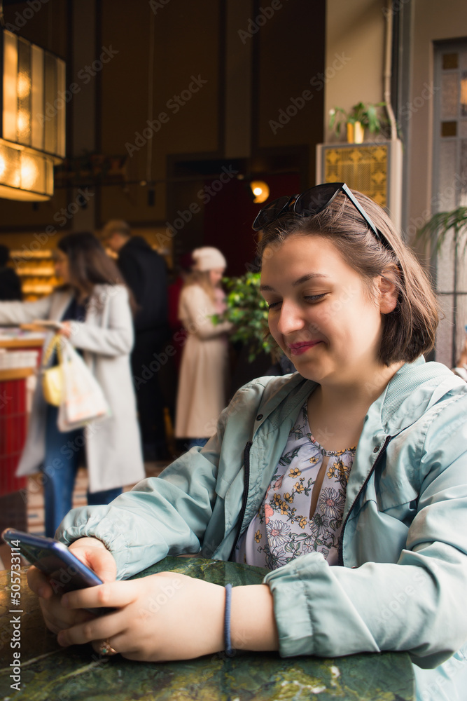 Young adult sitting at the table holding smartphone in shop. Vertical. Young adult sitting at the table holding smartphone in shop. Vertical.