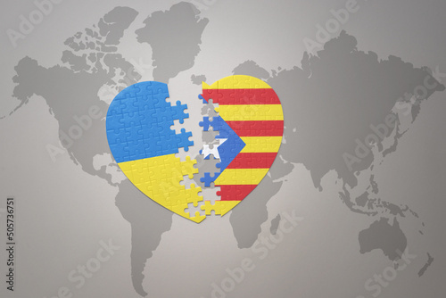 puzzle heart with the national flag of ukraine and catalonia on a world map background. Concept. photo