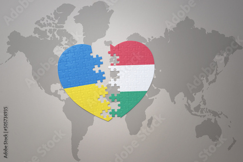 puzzle heart with the national flag of ukraine and hungary on a world map background. Concept.