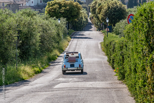 Fotografie A vintage Italian Fiat 500 convertible car drives along a typical Tuscan tree-li