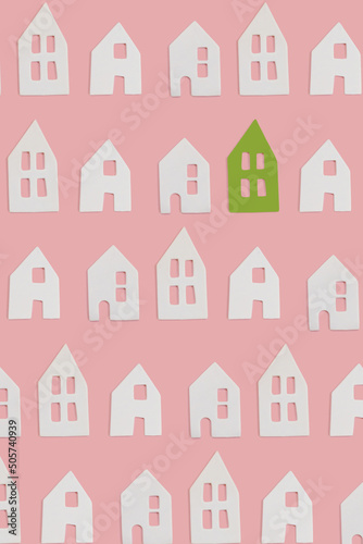 White and one green small decor ceramic houses with windows on pink flat lay background. Minimal creative card or wallpaper idea. Top view pattern. Stand out concept.