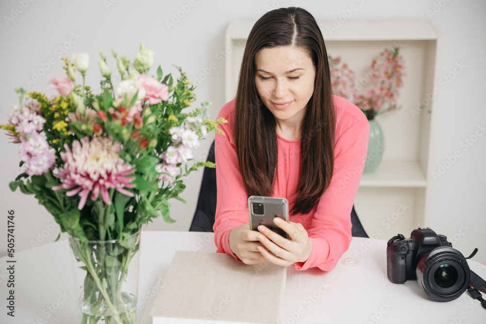 Photographer stands at the table and looks at something in the cell phone. Social media for photographers. Write messages on the cell phone Photographer stands at the table and looks at something in the cell phone. Social media for photographers. Write messages on the cell phone
