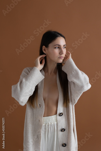 Fashion beauty portrait of young woman with long hair in beige knitted cardigan on brown background