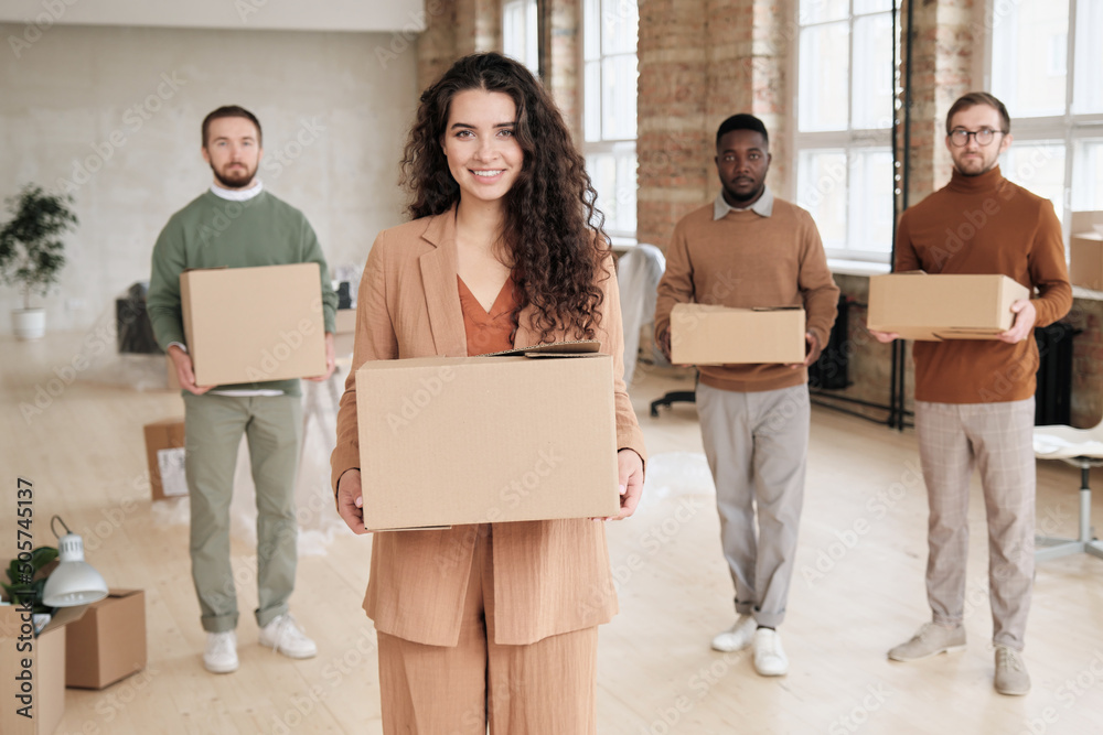 Portrait of smiling attractive business owner and her employee carrying moving boxes while leaving old office Portrait of smiling attractive business owner and her employee carrying moving boxes while leaving old office