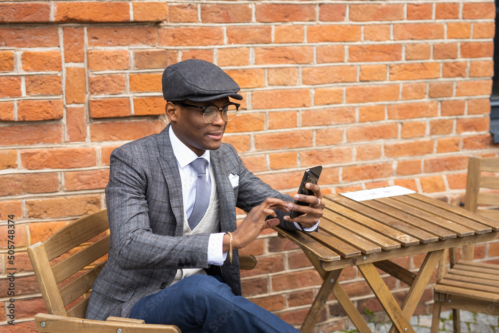 portrait of stylish african man with phone on brick wall background