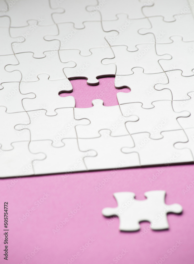 incomplete white puzzle with mauve background. the matching piece is outside the puzzle, vertical image with copy space. incomplete white puzzle with mauve background. the matching piece is outside the puzzle, vertical image with copy space.