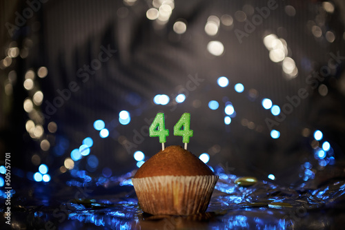 Holiday or birthday digital greeting card concept. Tasty vanilla cupcake or muffin with number 44 forty four on aluminium foil and blurred bright background. High quality photo photo