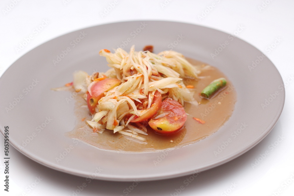 Thai papaya salad on a plate, papaya salad with poop, lime, pepper, red tomatoes in a gray plate on a white table. Thai papaya salad on a plate, papaya salad with poop, lime, pepper, red tomatoes in a gray plate on a white table.
