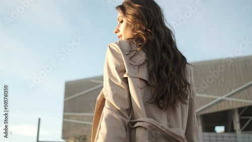 Young beautiful girl walks on the street. Brunette with long hair in a black hat and a brown cloak. Portrait frame from the back