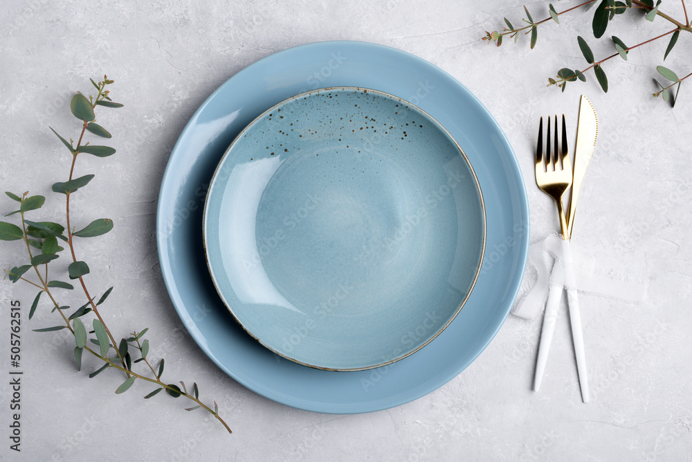Φωτογραφία Festive table setting with blue ceramic plate, golden cutlery set and fresh eucalyptus leaves on grey concrete table top view