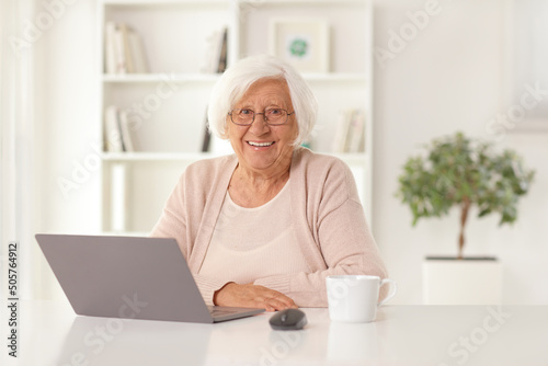 Happy elderly woman sitting at home with a laptop computer