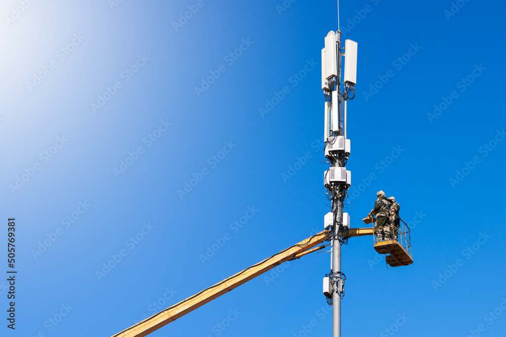 Modernization of the cell tower. Two service engineers work at a height. Copy space.