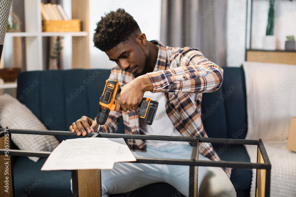 Φωτογραφία Portrait of happy african american man in casual attire with cordless screwdriver in his hand assembling modern cupboard at living room