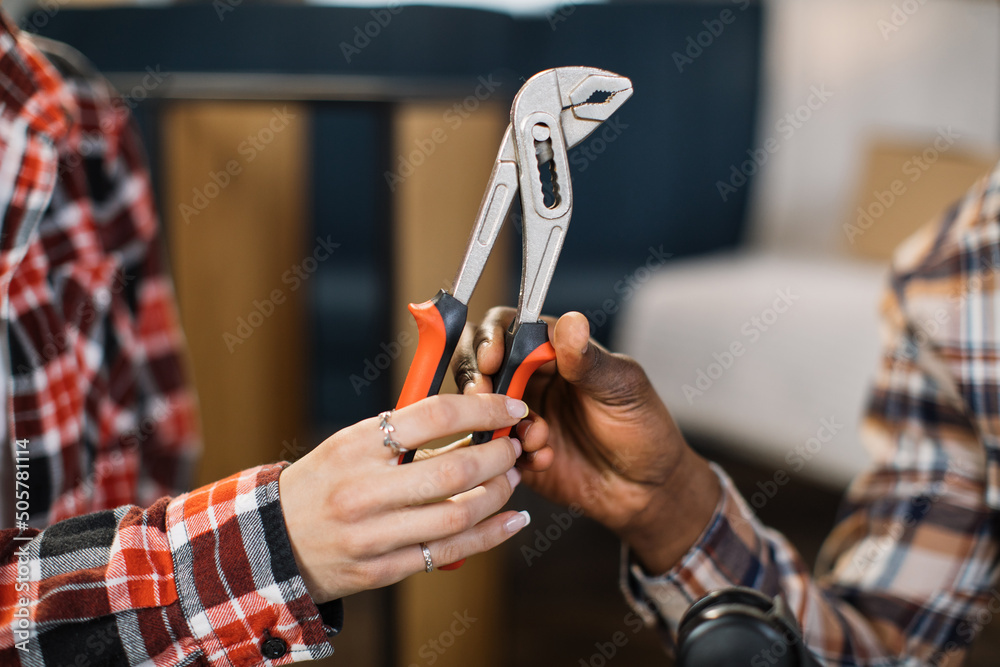 Close up of caucasian woman giving pliers to african american man at living room. Happy wife assisting husband during furniture assembly. Moving concept.