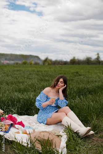 Beautiful young woman in a blue dress with makeup and pink flowers on a picnic in nature.