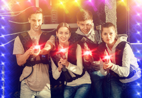 Happy young people with laser pistols posing together in bright beams in laser tag labyrinth. High quality photo