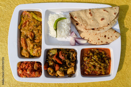 Indian Simple homemade lunch of Roti, sabji with mix veg brinjal potato curry and french beans curry, dal and gaajar halwa. complete simple home cooked meal thaali on white background photo
